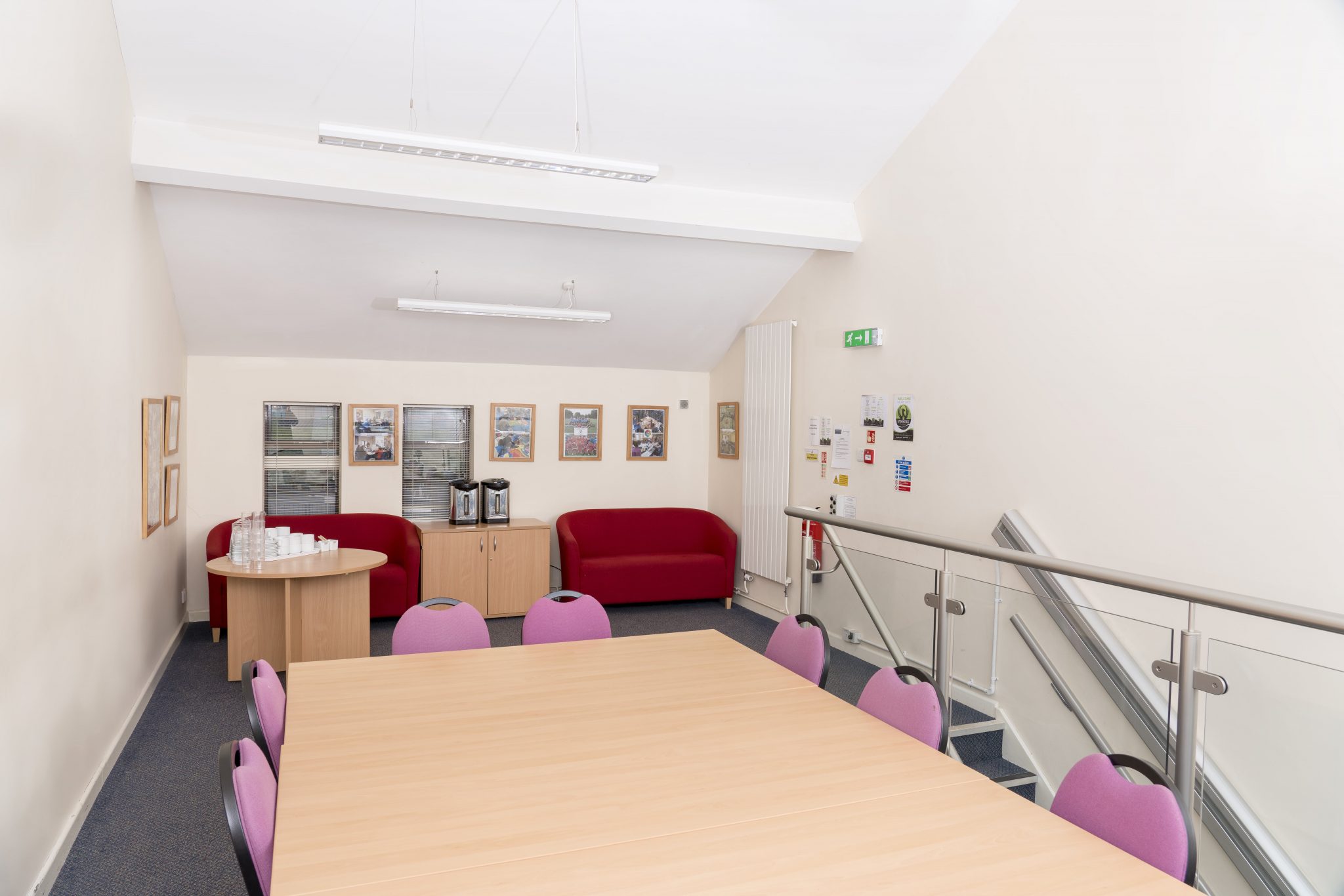 A large table is in the foreground, with 7 chairs around. Behind the table, there are two sofas and a table. Stairs up into the room can be seen in the right of the image.